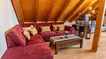 Ein Loft-Zimmer mit einem roten Ecksofa, einem Holztisch und einer Holzbalkendecke.
