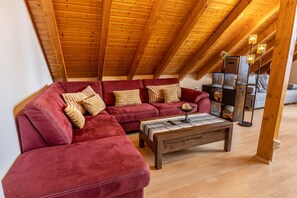 Un espace de vie de style loft avec un canapé d’angle rouge, une table basse en bois et un plafond en bois.