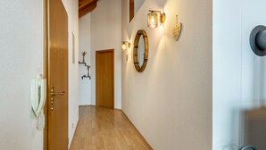 A hallway with wooden flooring, a wooden door, a wall-mounted telephone, and decorative wall sconces.