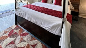 Ein Bett mit Baldachin, ausgestattet mit weißer und roter Bettwäsche, ein gemustertes Teppich und ein Nachttisch mit Lampe.