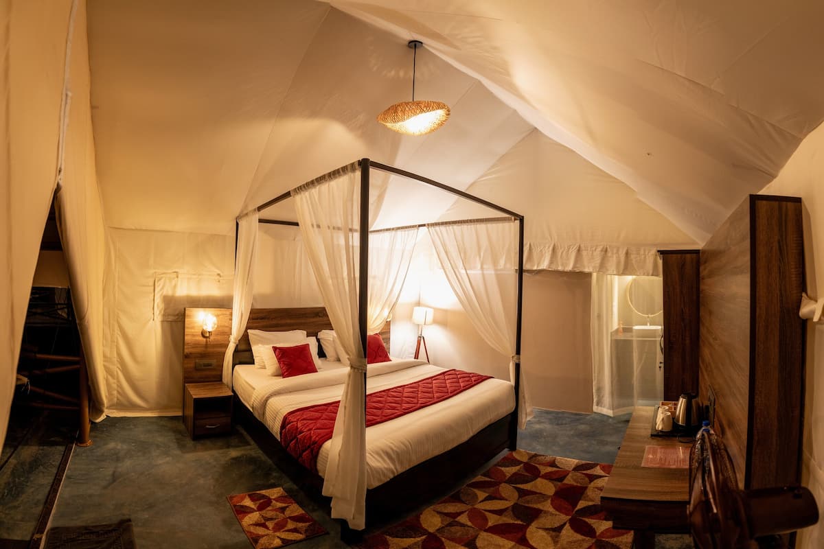 A four-poster bed with a canopy, a bedside table, a lamp, and a small table with a kettle and a cup.