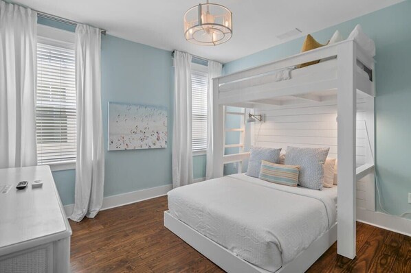 A bedroom with a bunk bed, a desk, and a large window with curtains.