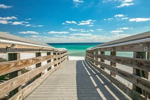 Un muelle de madera que conduce a una playa con agua turquesa cristalina y cielo azul.