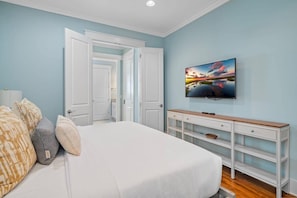 Un dormitorio con una cama, un televisor en la pared y un tocador blanco.