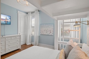 A bedroom with a bed, a dresser, a painting, and a window with blinds.