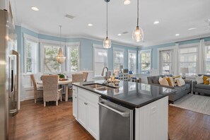 A modern kitchen with a central island, white cabinetry, and a dining area with wicker chairs.