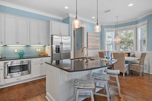A modern kitchen with white cabinets, a stainless steel refrigerator, a built-in microwave, and a large island with bar stools.