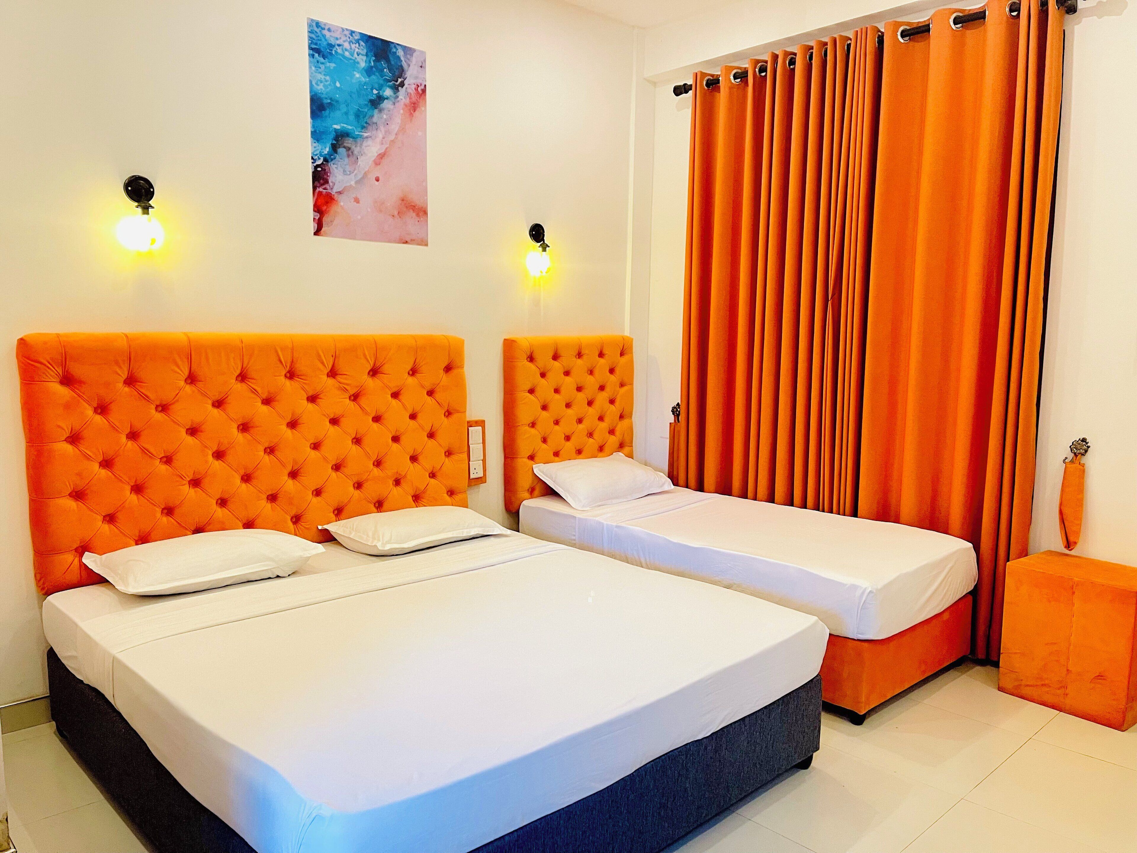 A room with two beds, each with an orange headboard, white bedding, and a small orange ottoman.