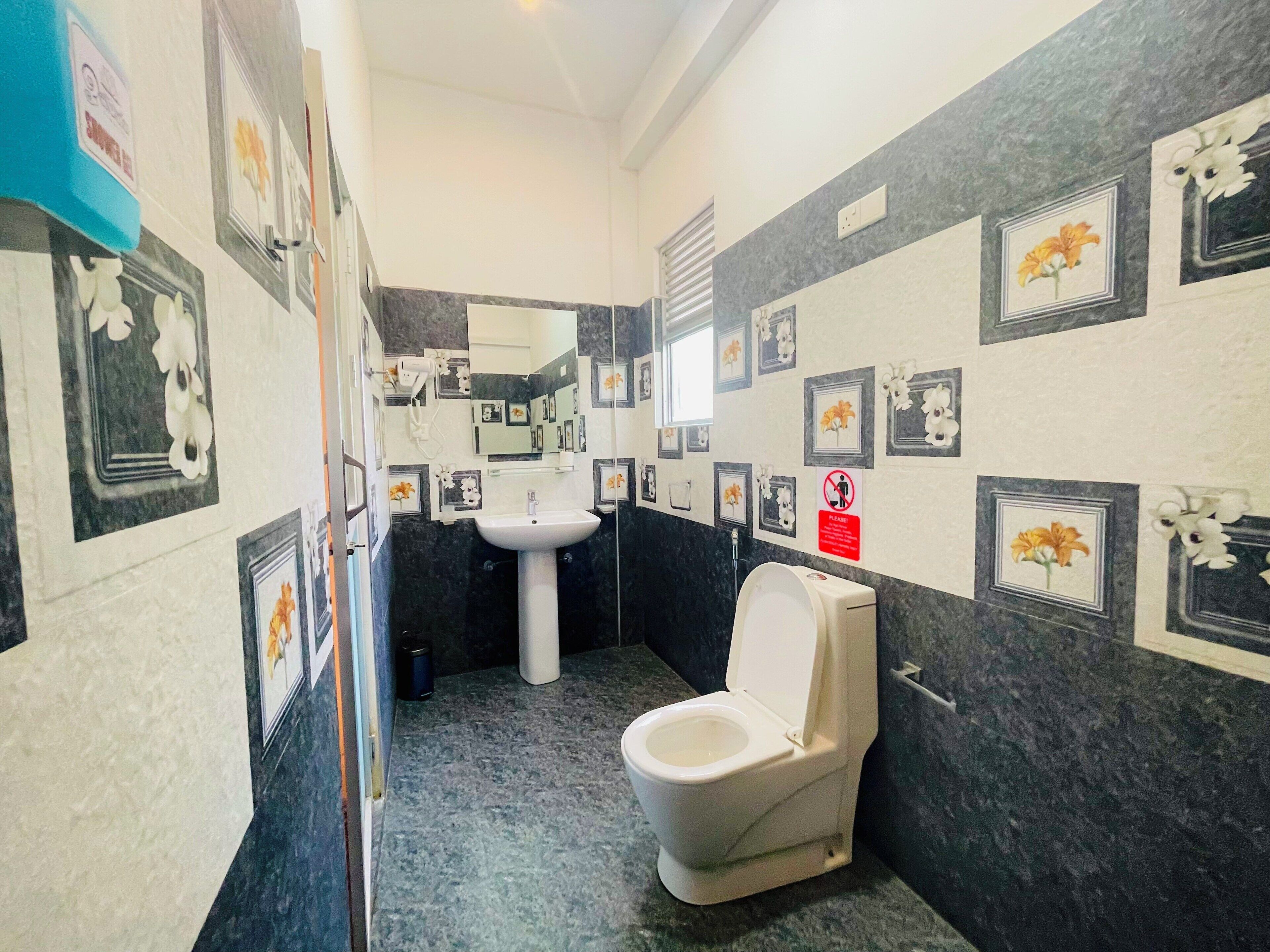 Un baño con inodoro, lavabo y espejo. Las paredes están decoradas con cuadros de flores.