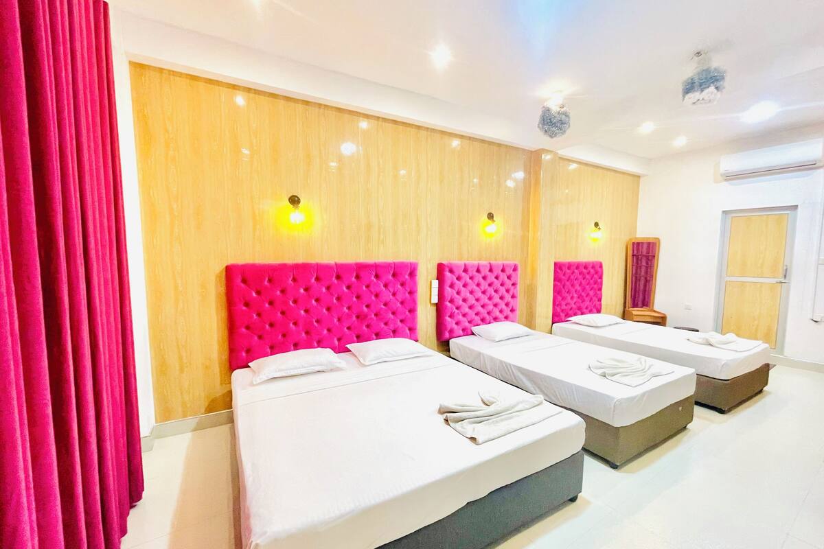 Een hotelkamer met drie bedden, elk voorzien van een roze hoofdbord en witte beddengoed.