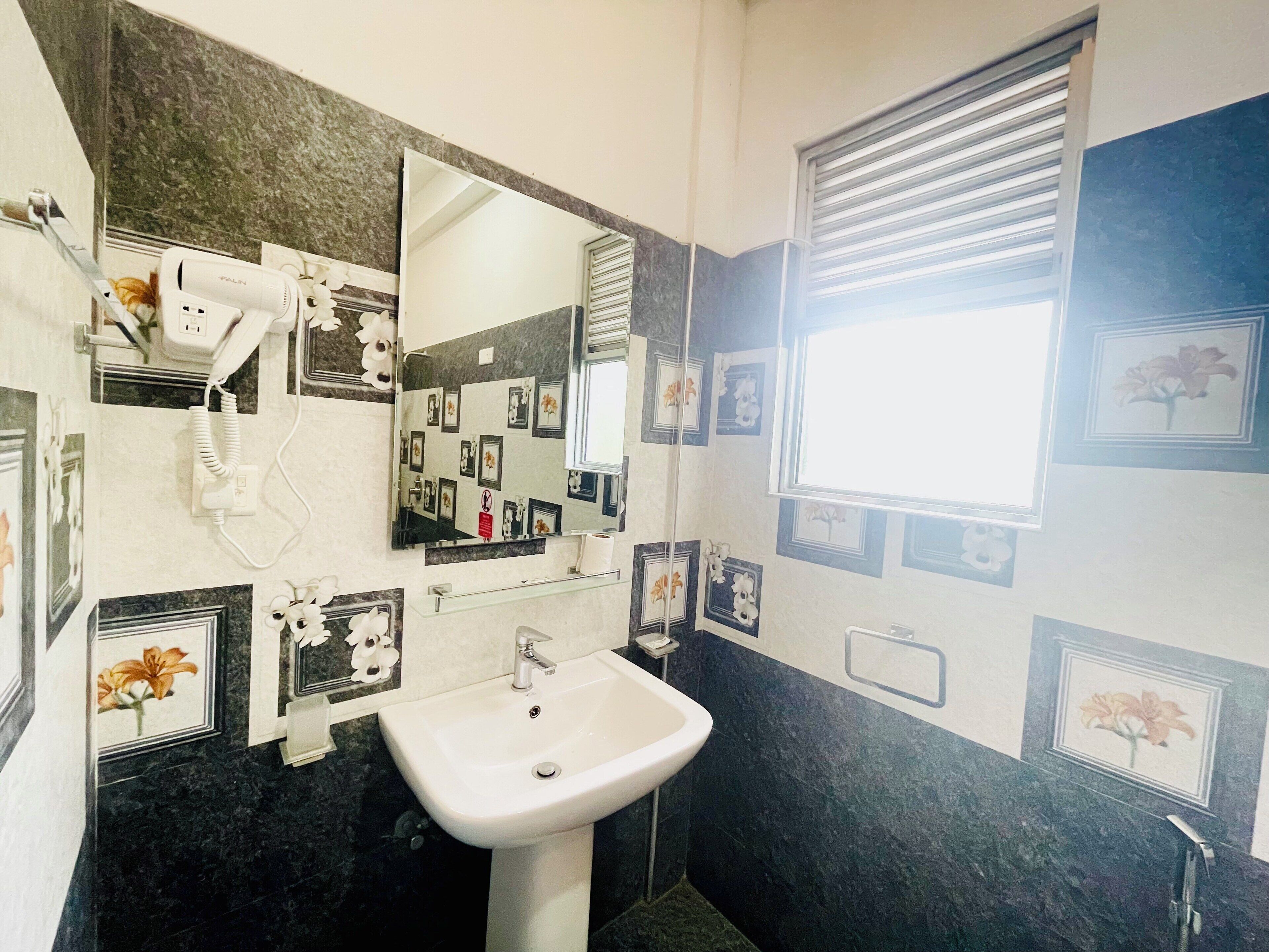 Une salle de bain avec un lavabo blanc, un miroir, un sèche-cheveux et des tableaux encadrés accrochés aux murs.
