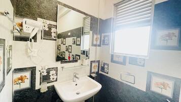 Une salle de bain avec un lavabo blanc, un miroir, un sèche-cheveux et des tableaux encadrés accrochés aux murs.