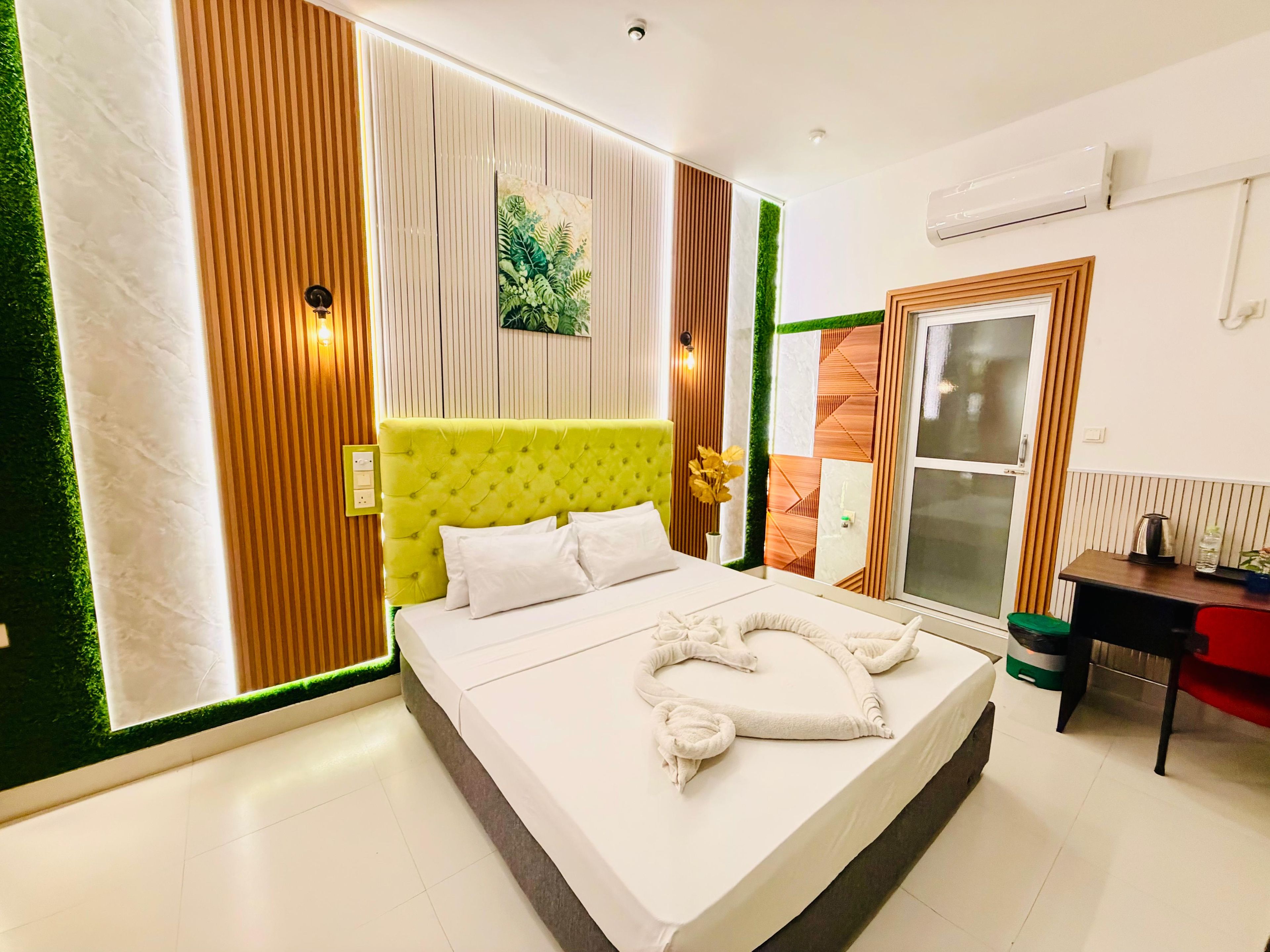 Un dormitorio moderno con un cabecero tapizado en verde, una cama con ropa de cama blanca y una decoración de toallas.