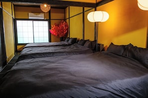 A hotel room with three beds, a large window, and a traditional Japanese-style lamp.