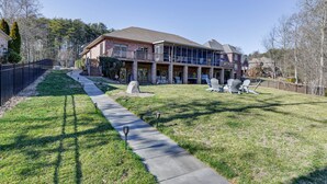 A two-story house with a covered porch, a lawn, and outdoor furniture. - Waterfront Lake Norman Retreat w/ Dock + Hot Tub! (Terrell)