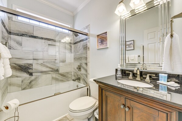 Un baño moderno con ducha envuelta en vidrio, inodoro blanco, tocador de madera con lavamanos y un espejo grande.