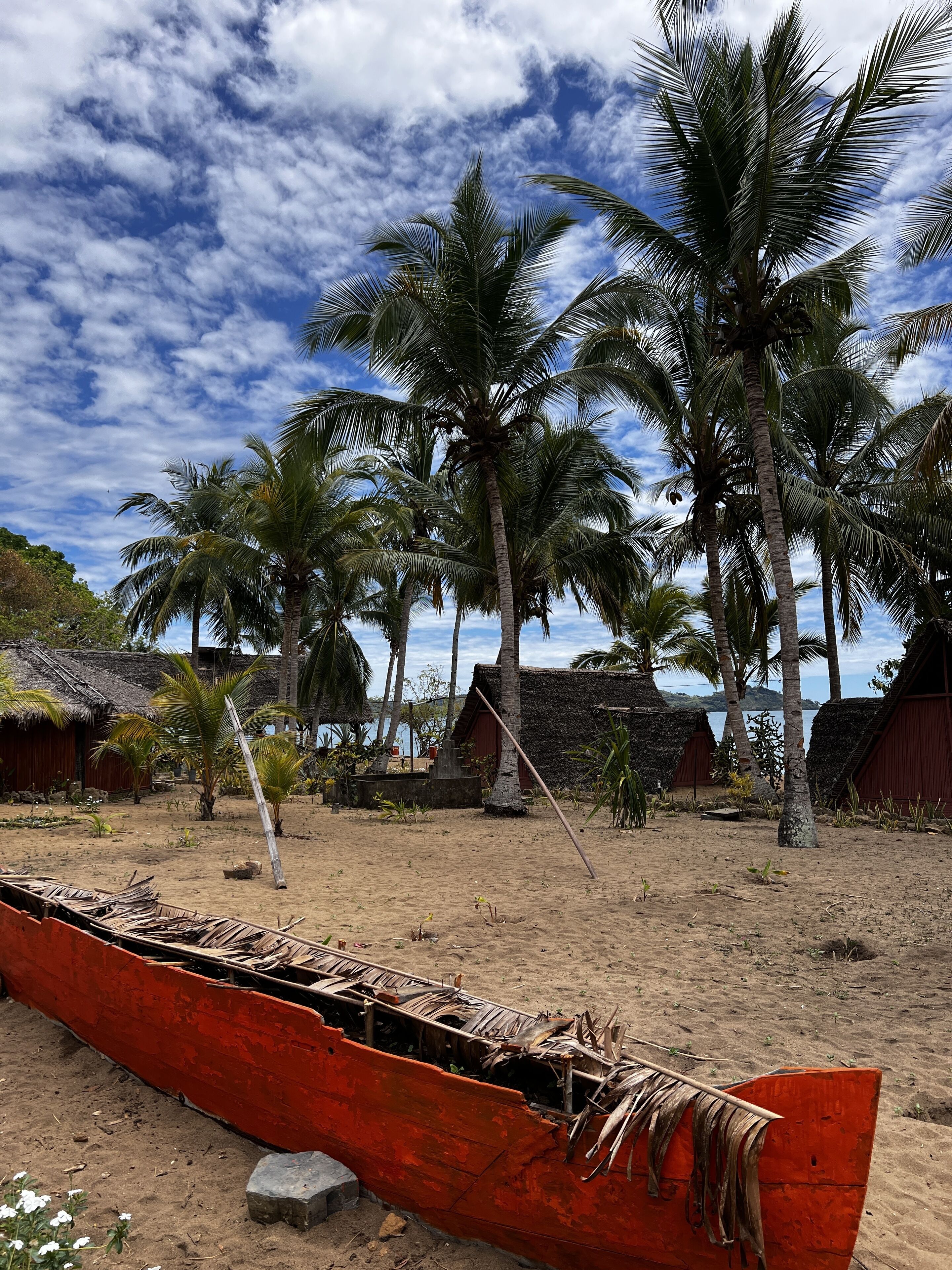 Escena de playa con un bote rojo, palmeras y chozas de techo de paja.