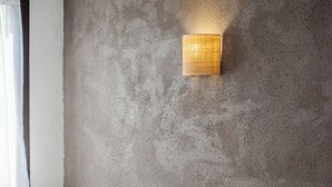 A hotel room with two beds, a white chair, a textured wall, and a wall-mounted light fixture. - Hôtel la Tour des Anglais (Mayenne)