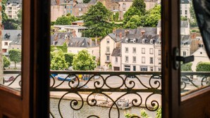 A view through a window with a wrought iron balcony railing, overlooking a town with buildings and a church steeple. - Hôtel la Tour des Anglais (Mayenne)