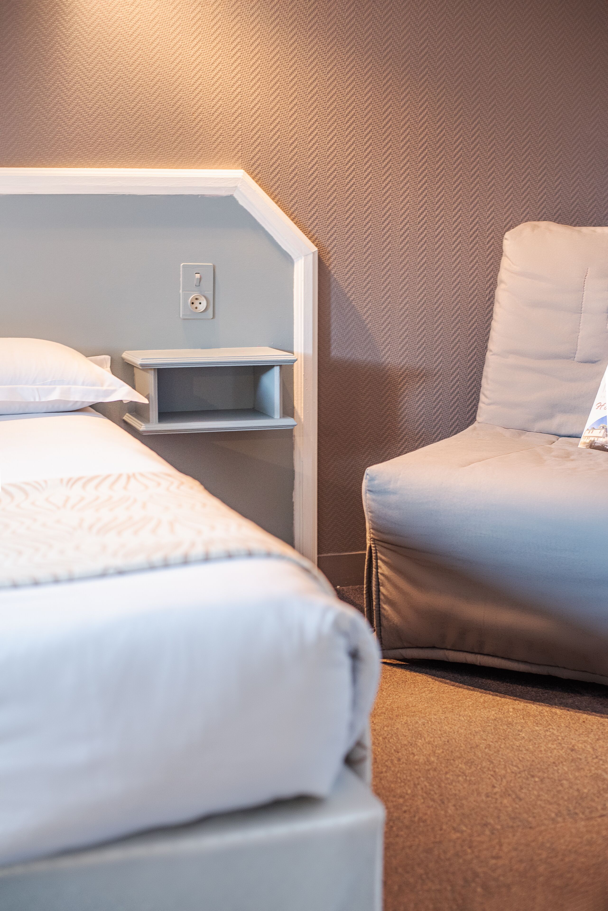 Hotelkamer met een bed, een stoel, een nachtkastje en een muur met een herringbone motief.