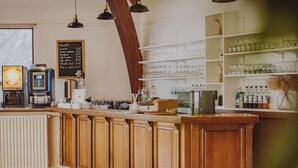 A bar area with wooden cabinets, a coffee machine, and shelves with glasses and bottles. - Hôtel la Tour des Anglais (Mayenne)