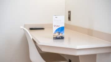 A white desk with a remote control and a brochure titled "Hotel".