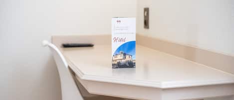 Un bureau blanc avec une télécommande et une brochure intitulée « Hôtel ».