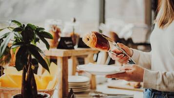 A person holding a croissant and a plate, with a potted plant and a table in the foreground.
