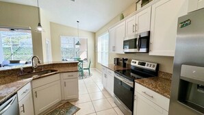 A kitchen with white cabinets, a granite countertop, a stainless steel refrigerator, a microwave, an oven, and a sink. - Sunshine 3bdrm pool house near Disney (Kissimmee)