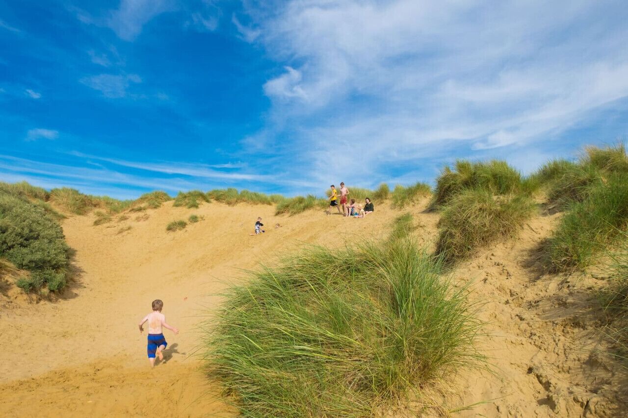 Una playa arenosa con dunas y vegetación dispersa.
