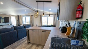 Et moderne køkken med en central ø, et spiseområde med sofa og en opholdsstue med tv.