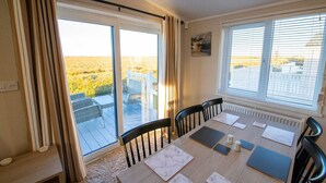 Spiseområde med et bord dækket til fire personer, store vinduer og udsigt over et mark.