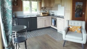 Une cuisine compacte avec un coin repas, comprenant une table ronde, deux chaises, un fauteuil blanc et une fenêtre laissant entrer la lumière naturelle.