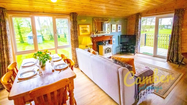 A wooden interior with a dining table set for four, a sofa, and a television. - Rainbow Petty - Pine lodge - Kent countryside (Brookland)