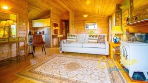A cozy cabin interior with a wooden ceiling, a white sofa with patterned cushions, a dining table, and a kitchen area. - Rainbow Petty - Pine lodge - Kent countryside (Brookland)