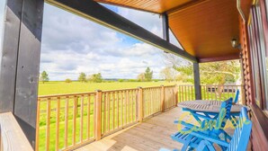 A covered outdoor deck with a wooden railing, a table, and blue chairs. - Rainbow Petty - Pine lodge - Kent countryside (Brookland)