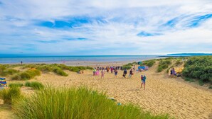Ein Strand mit Menschen, grasbewachsenen Dünen und blauem Himmel.