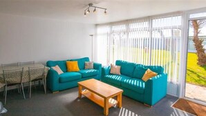 Ein Wohnzimmer mit einem Salonzug in Türkis, einem Holztisch und einem Essbereich mit einem gemusterten Tischläufer.