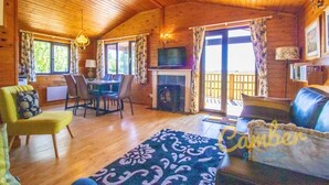 L’intérieur d’un chalet accueillant, avec des murs en bois, un coin repas, un salon doté d’un canapé et d’un tapis à motifs, et un téléviseur posé sur un meuble.