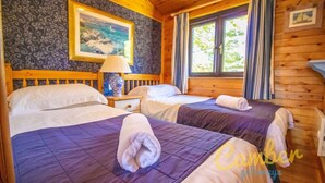 Une chambre avec deux lits, une table de chevet, une lampe, un tableau et une fenêtre avec des rideaux.