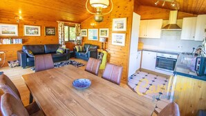 L’intérieur chaleureux d’un chalet avec une table à manger en bois, des sièges en cuir, une cuisine dotée de meubles blancs et des tableaux encadrés accrochés aux murs.