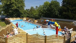 Un área de piscina con varias piscinas, cercas de madera y sillas de descanso.