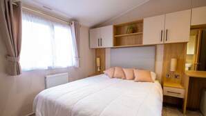 Un dormitorio con una cama grande, una mesita de noche, un armario y una ventana con cortinas.