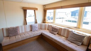 A corner sofa with striped cushions, a wooden floor, and large windows with curtains.