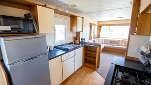 Una cocina compacta equipada con microondas, refrigerador y estufa.  Cuenta con un pequeño comedor con mesa y sillas.