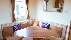 A cozy RV interior with a round table, cushioned seating, and a window with curtains.