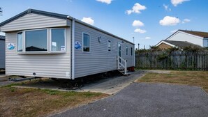 A mobile home with a ramp leading to the entrance, a fenced yard, and a clear sky.