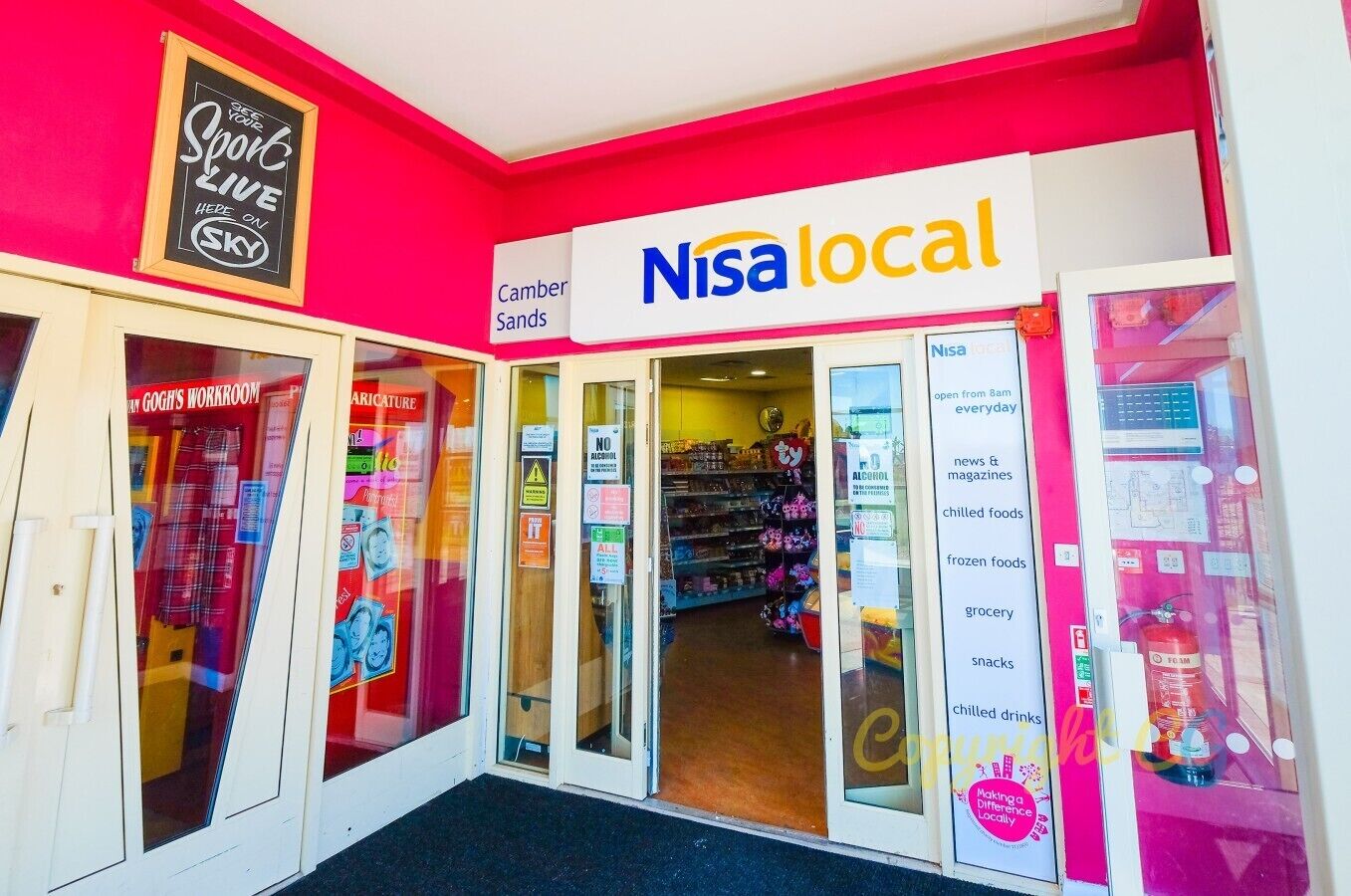 A storefront with a bright pink wall, a sign for 'Nisa local' indicating a local news and grocery store, and a 'Camber Sands' sign above the entrance.