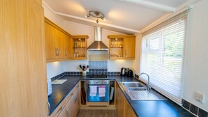 Una cocina compacta con armarios de madera, horno empotrado, un lavamanos y una ventana con persianas.