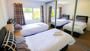 Habitación de hotel con tres camas, un espejo grande y una ventana con cortinas.
